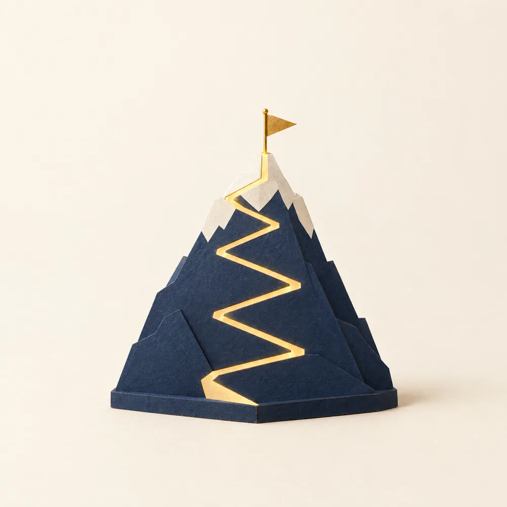 Maqueta de papel: una montaña con una ruta dorada continua hasta una bandera en la cumbre